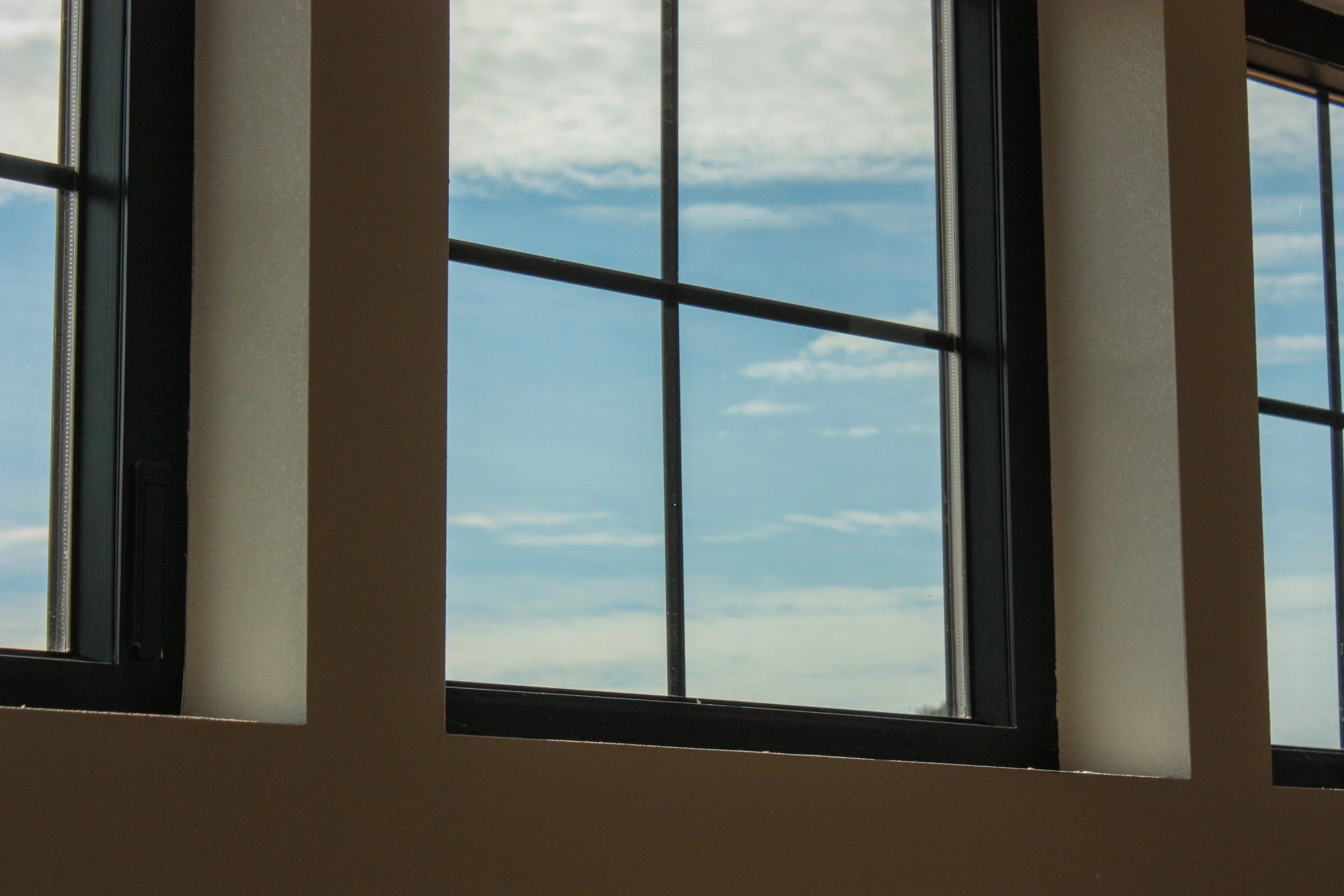 Looking through a window with a black frame, showing a view of a blue sky with scattered clouds.