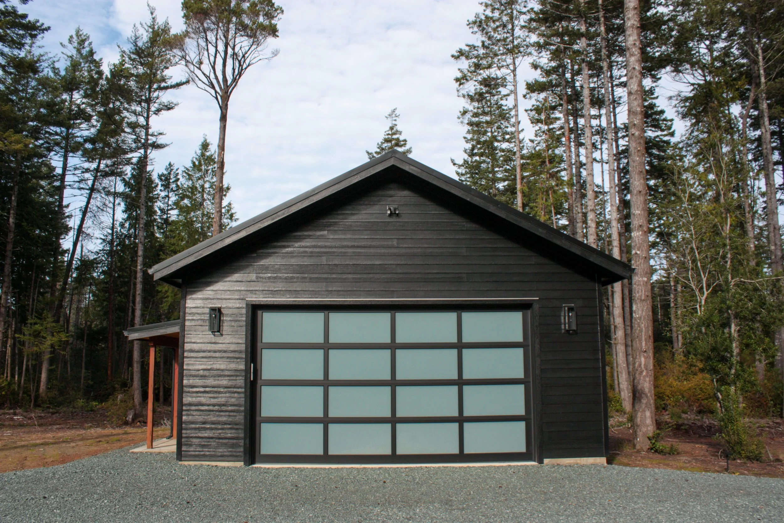 Black garage with frosted glass doors in a forest setting with tall trees and cloudy sky.