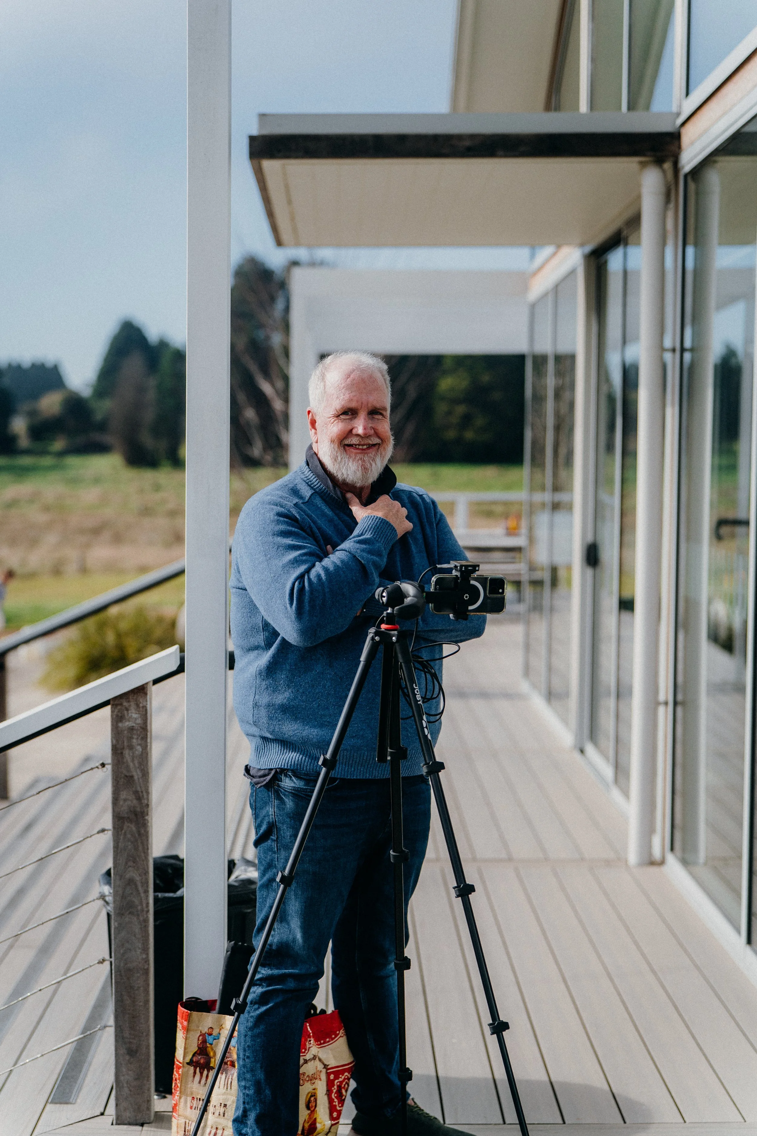 Darren Youens, the curator of Left Field Property News smiling at the camera, with a camera mounted on a tripod.
