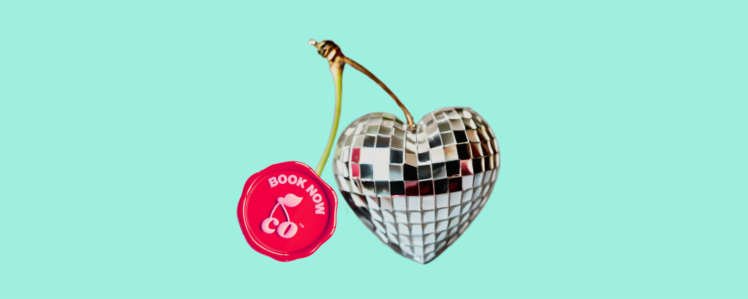 A cherry with a green stem and a mirrored disco ball heart on a bright pink background.