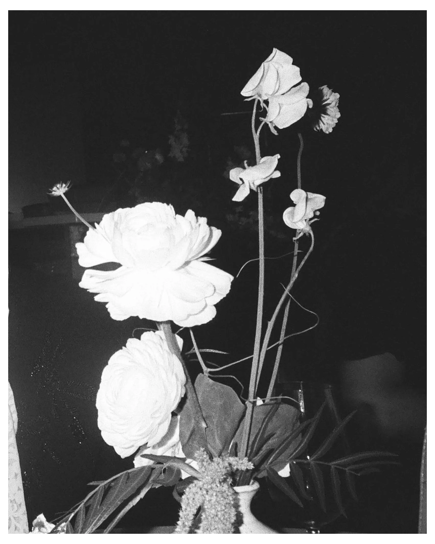 A black and white image of a flower arrangement with large blossoms, leaves, and smaller flowers or buds.
