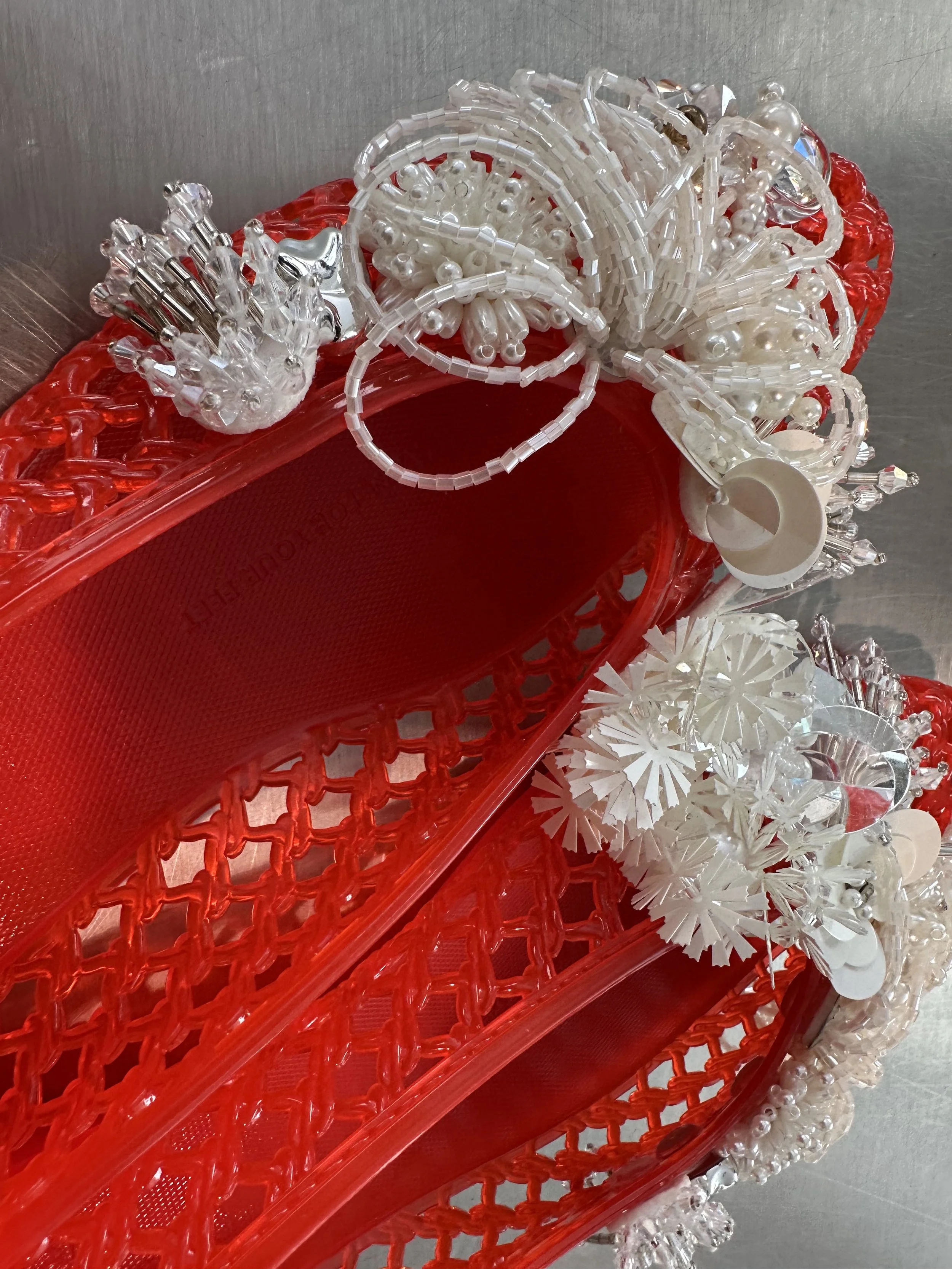 A collection of various clear and white plastic jewelry and accessory pieces, including beads, pearls, and intricate decorative elements, organized in a red plastic bin.