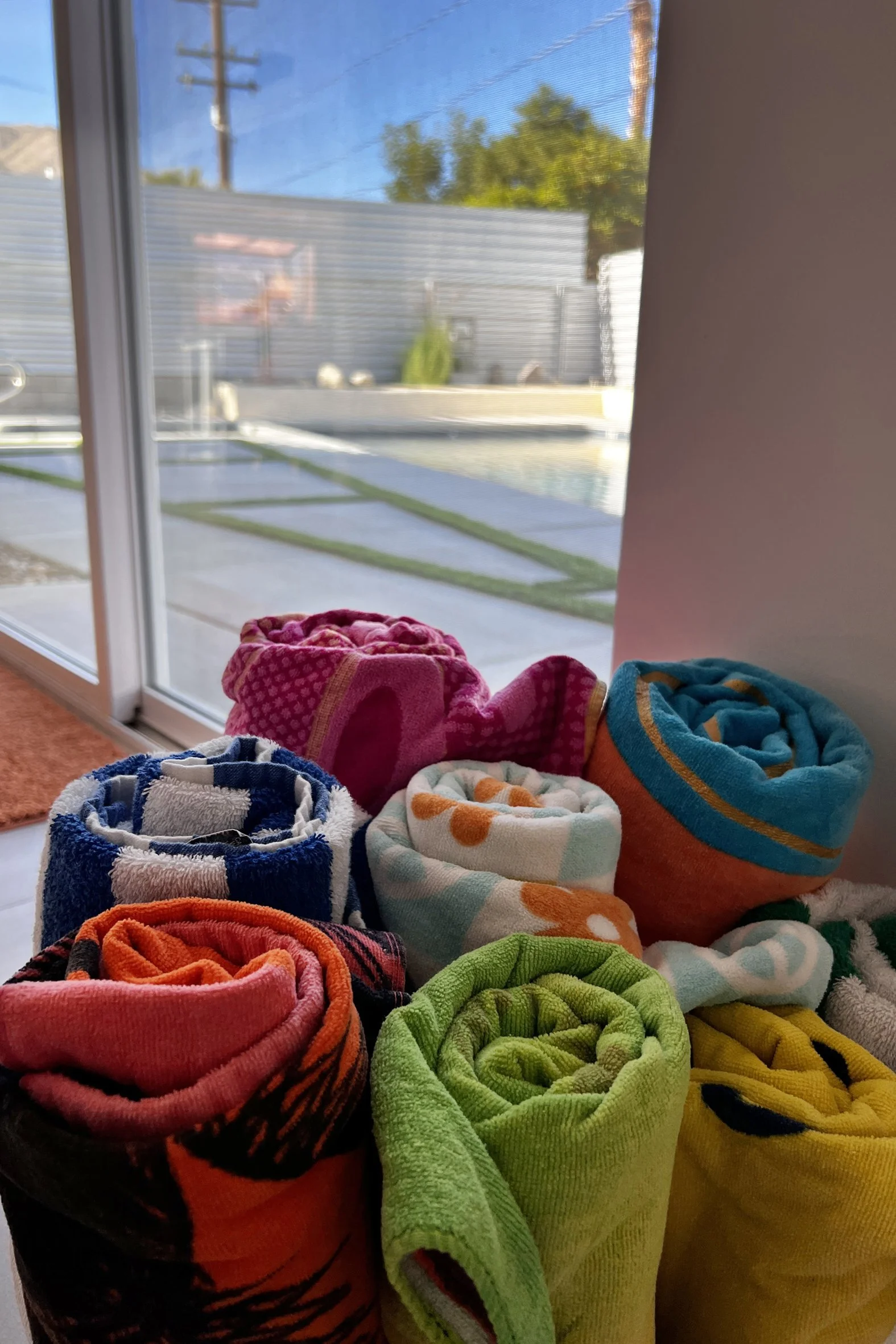 A collection of colorful rolled towels near a large window with a backyard view.