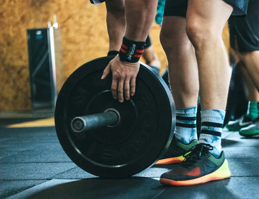 Person lifting a barbell with weights during a workout in a gym.