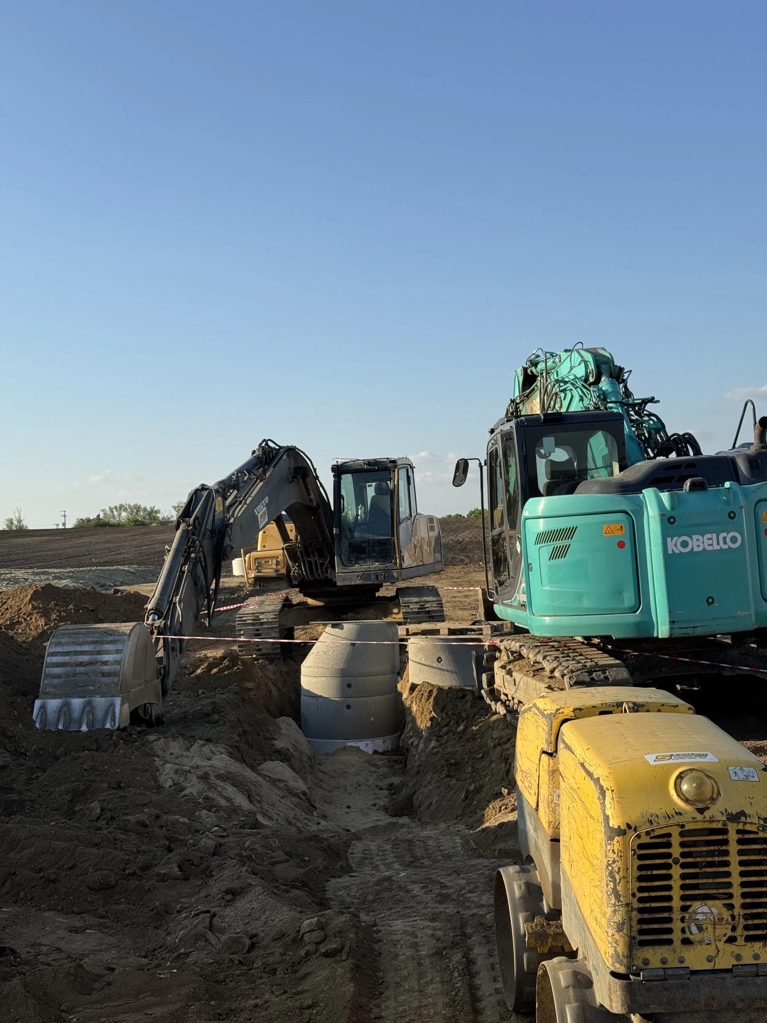 Construction site with excavators and a large pipe in the ground during daytime.