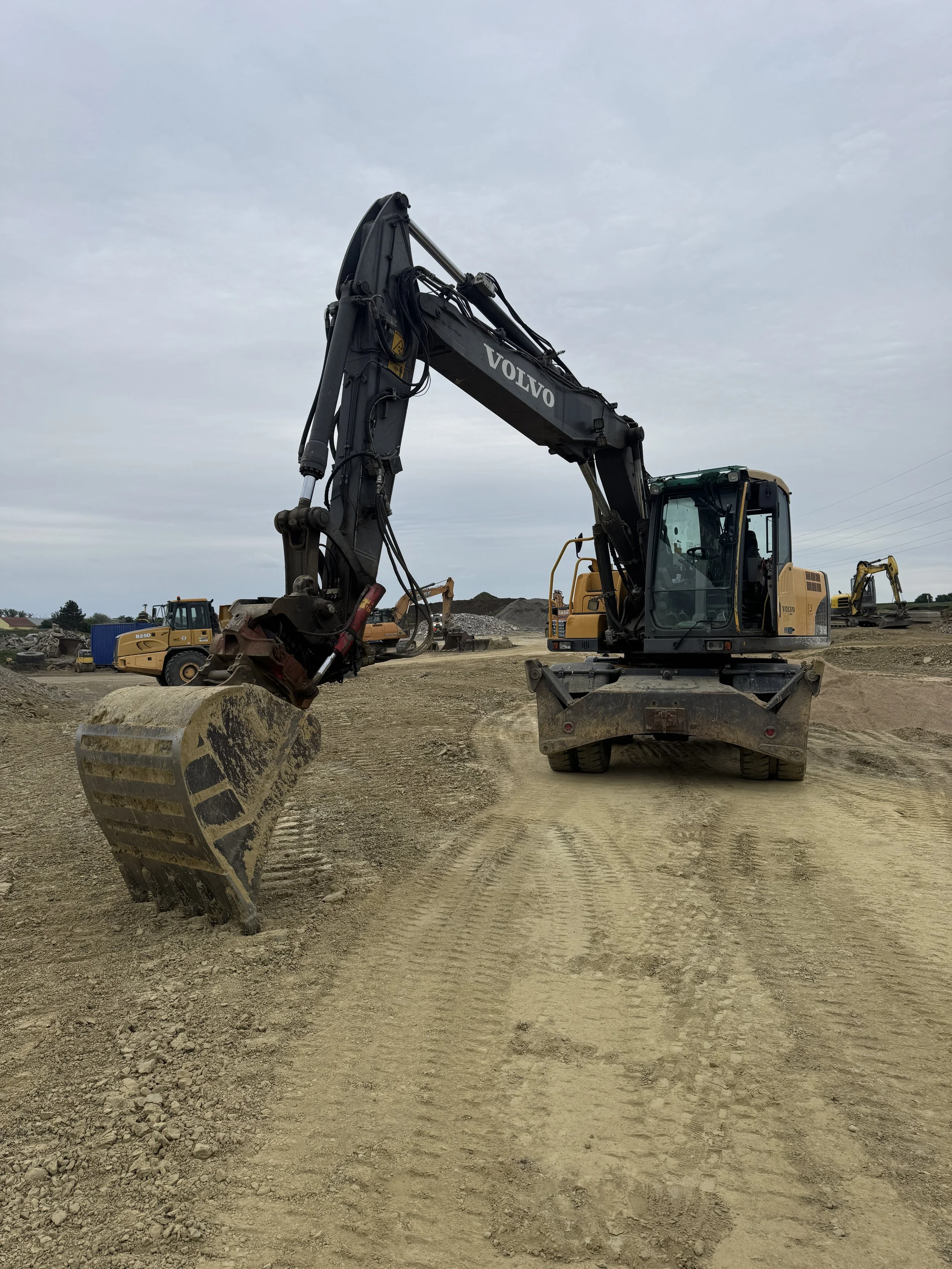 A large black and yellow excavator with the brand name Volvo on the arm, working on a construction site with dirt and other construction machinery in the background.