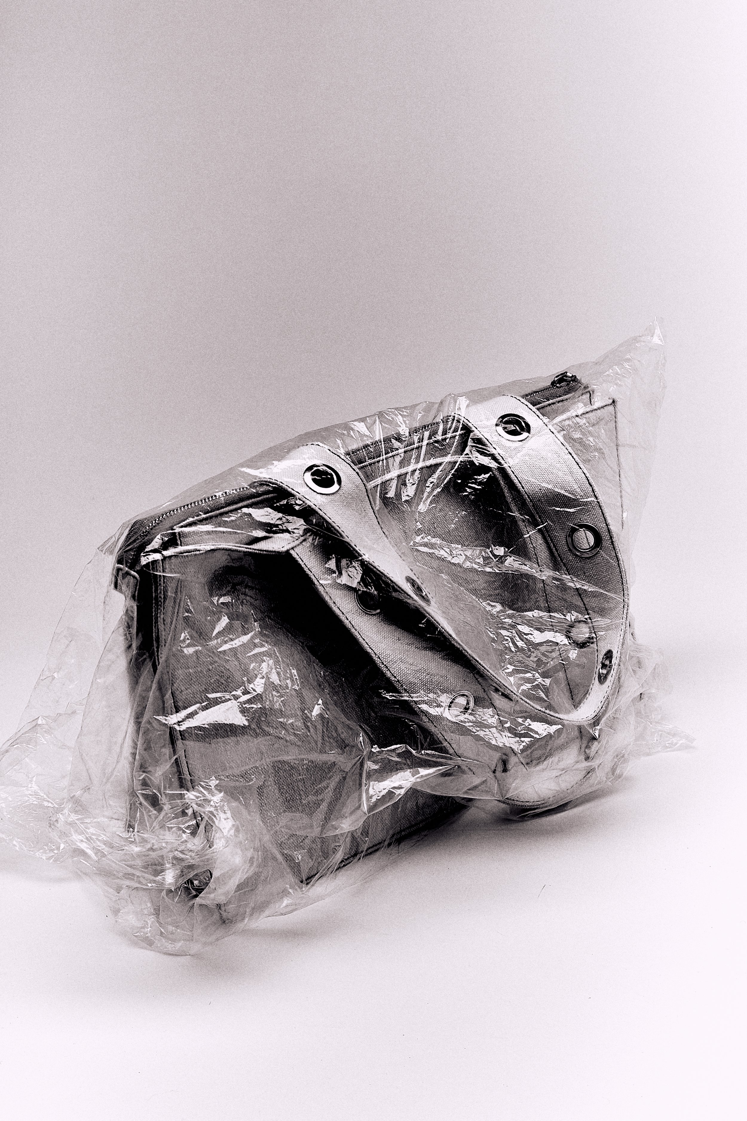 A small wrapped gift or item in shiny silver wrapping paper, partially covered in clear plastic, with black eyelet details.