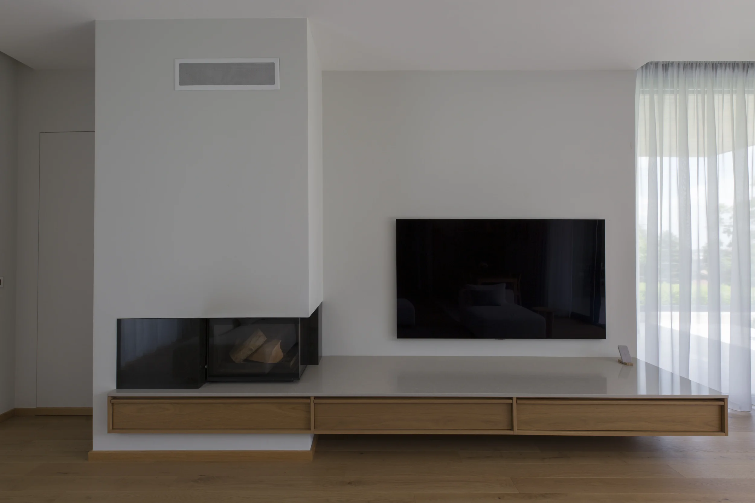 Platsbyggd TV-bänk och eldstad i trä och sten, en arkitektonisk helhet
