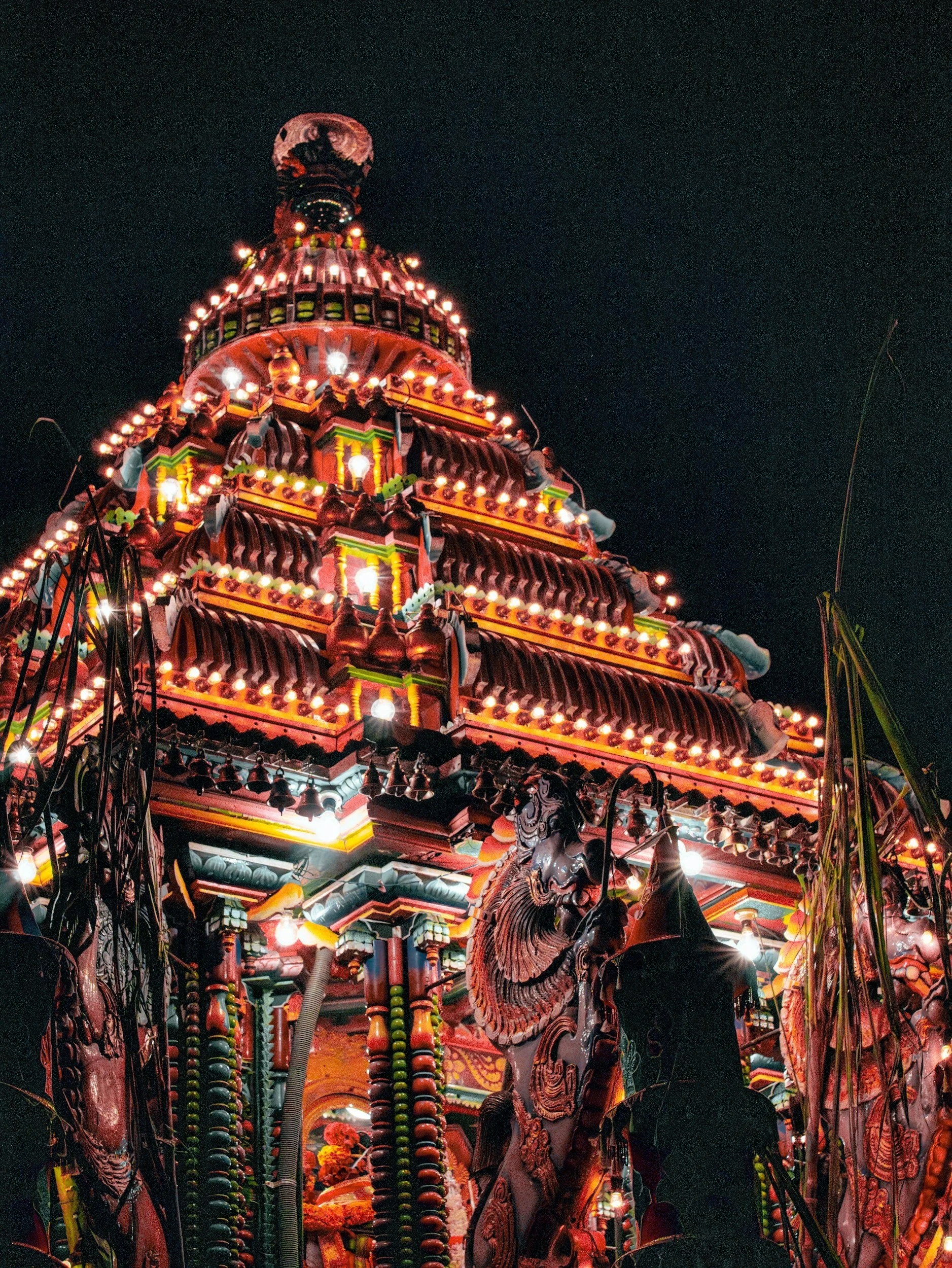A brightly lit, colorful carnival attraction at night with elaborate decorations, lights, and figures.