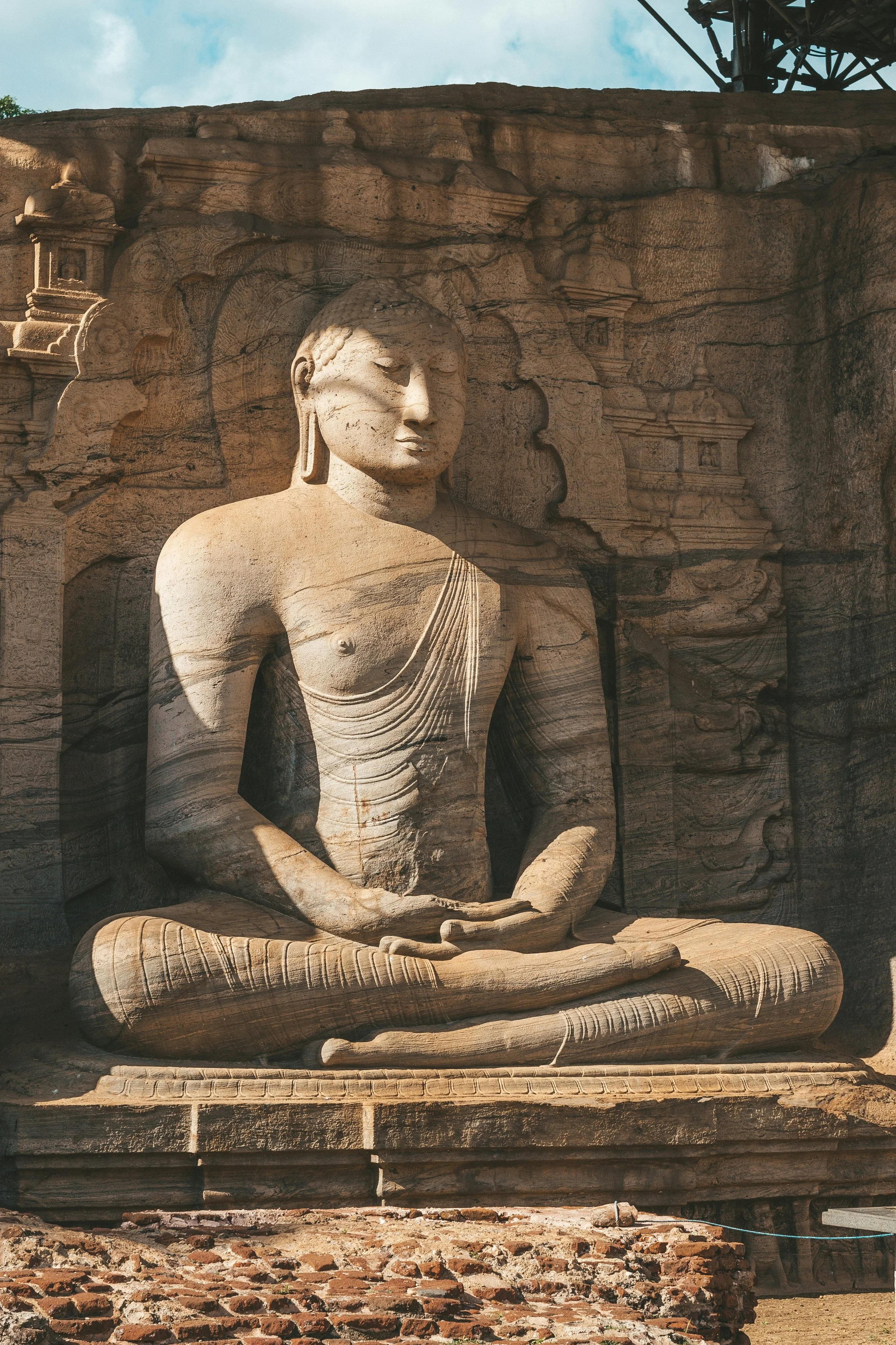 Sandstone sculpture of a seated, meditative Buddha carved into a large rock face, with intricate detailing and surrounding architectural carvings.