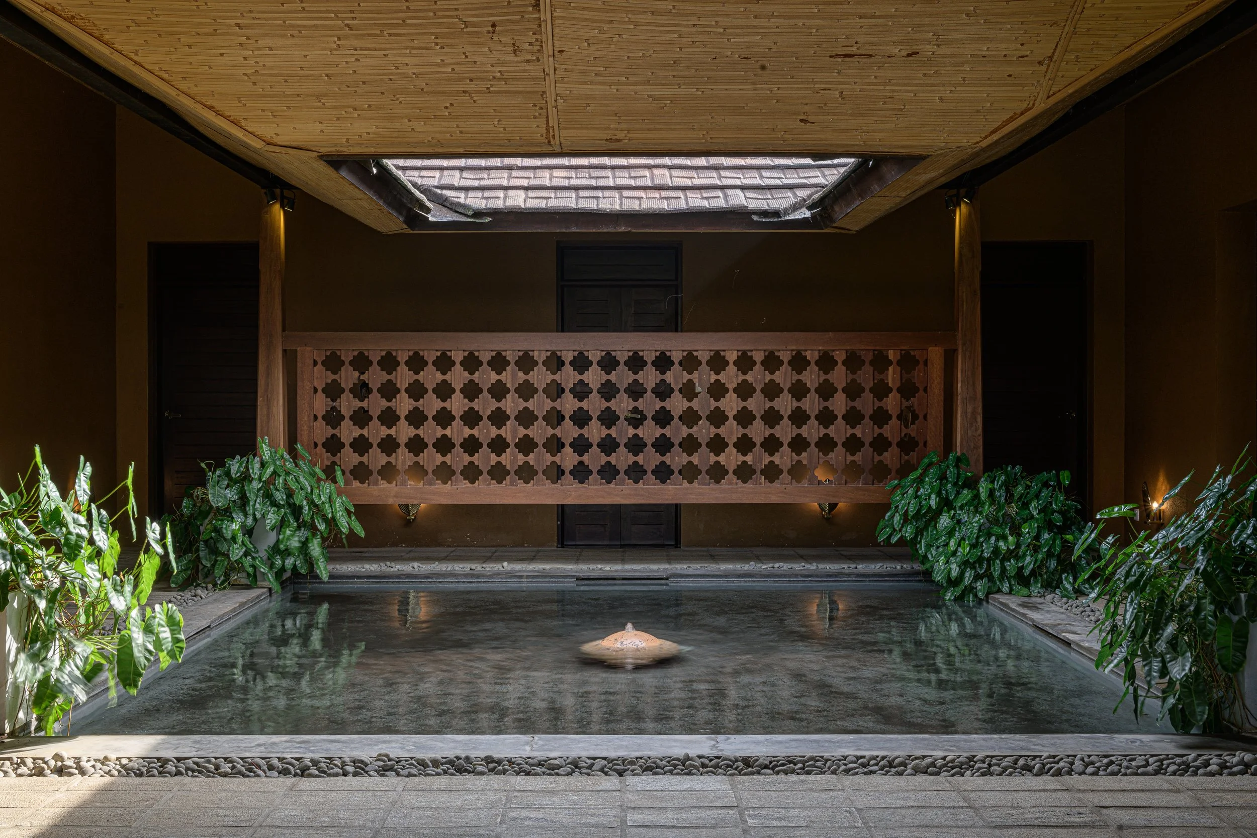 Indoor pool with fountain, plants on the sides, wooden railing, and a skylight in the ceiling.
