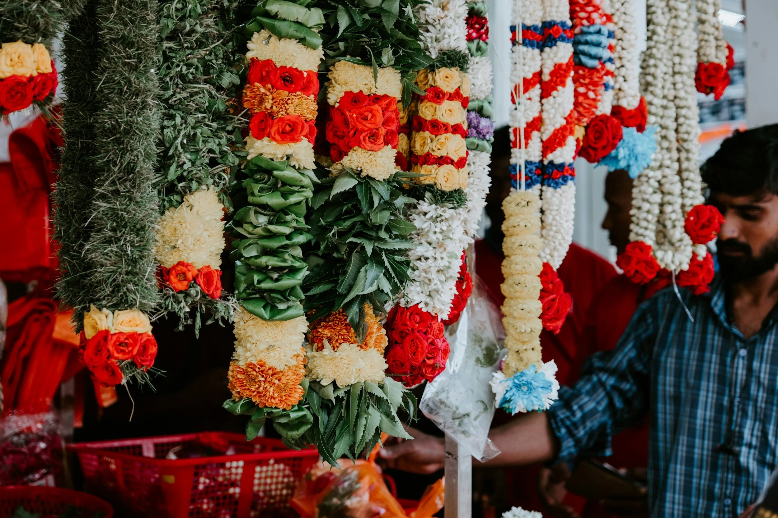 Flower garlands hanging at a market stall with people browsing.