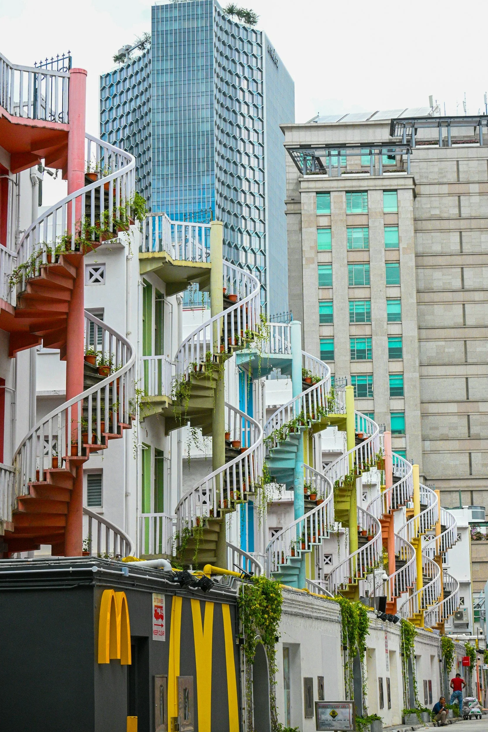 Colorful spiral staircases on a white building in an urban city with tall modern skyscrapers in the background.
