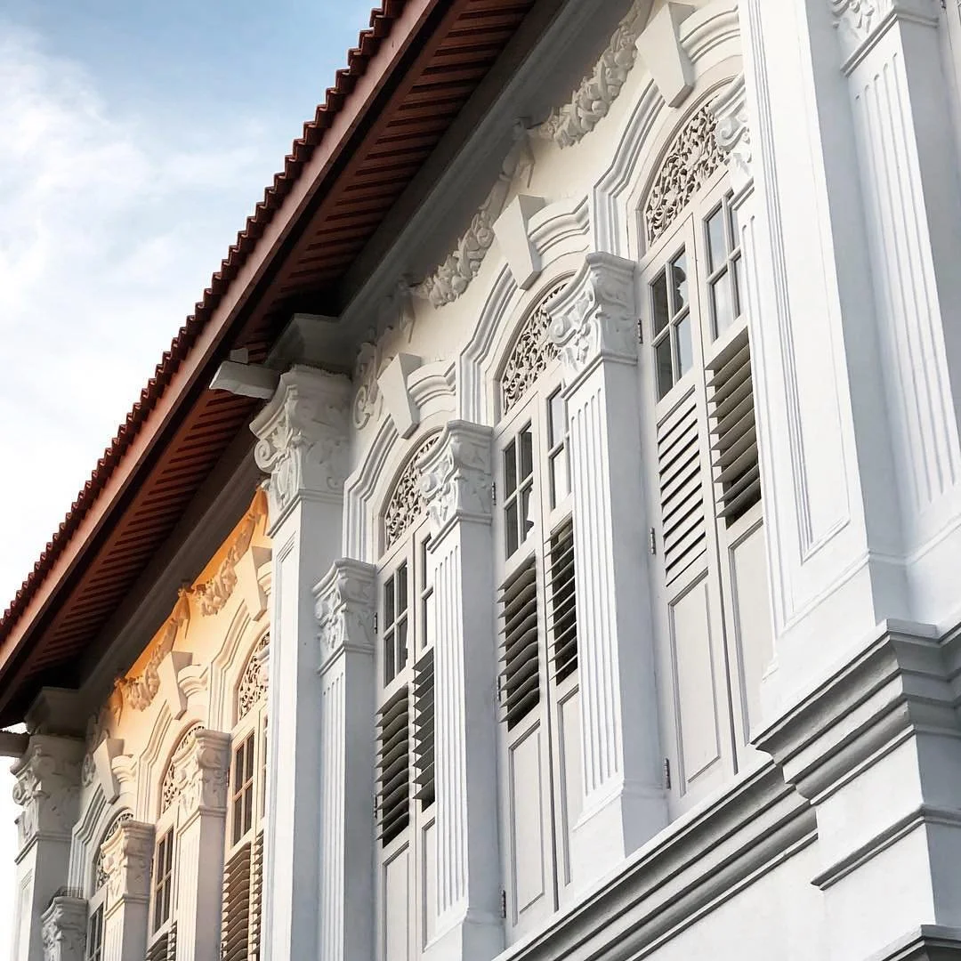 Close-up of a white colonial-style building facade with decorative window shutters and intricate architectural details under a red tiled roof.