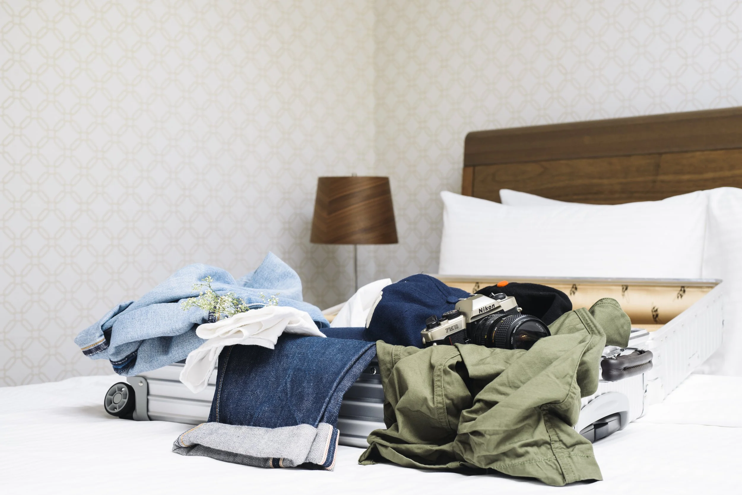 Unpacked suitcase on a bed with clothes and a camera, in a hotel room.