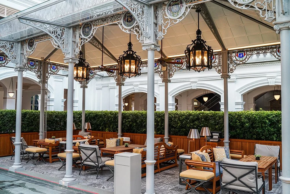 Outdoor patio with seating, tables, and lamps, surrounded by a hedge and topped with ornate metal and glass lanterns.