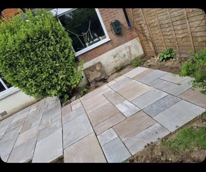 Newly laid outdoor patio with rectangular stone tiles next to a brick house, garden plants, and a wooden fence.