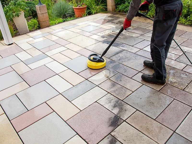 A person cleaning or sealing a stone patio with a powered cleaning or sealing device.
