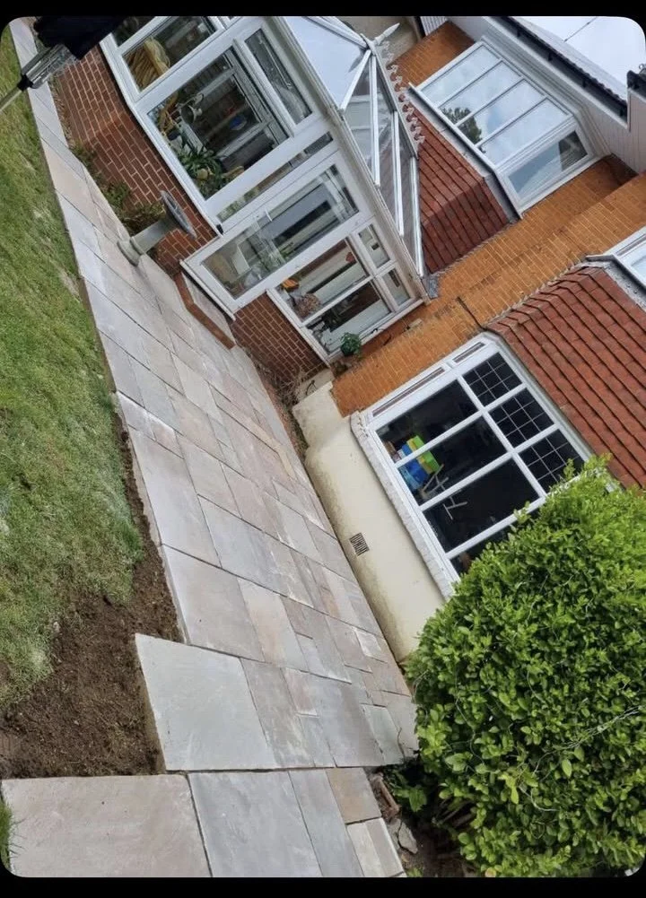 View of a backyard patio and house exterior with a brick wall, large windows, a glass door, and a small vegetable garden greenhouse.