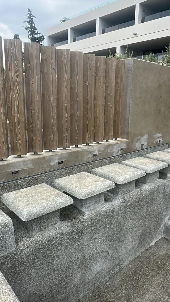 Concrete steps with square stone treads, a wooden fence, and a modern white building with balconies in the background.