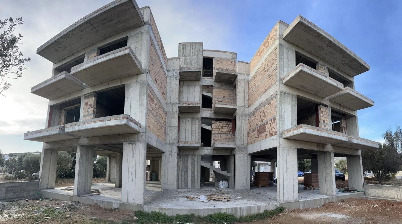 Under construction multi-story building with concrete and brick walls, open windows, and balconies.
