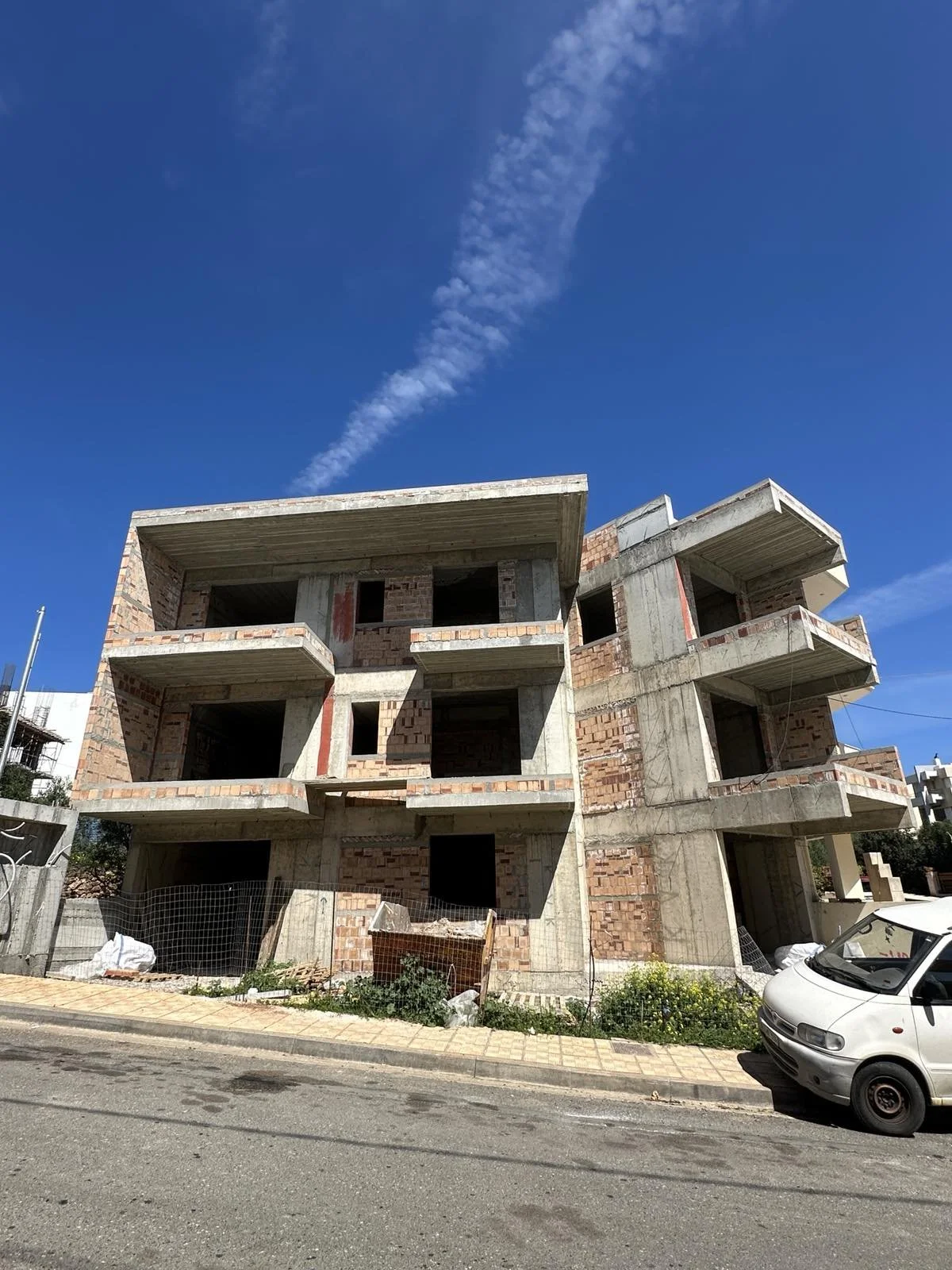 Under-construction brick and concrete multi-story building with blue sky and wispy clouds.