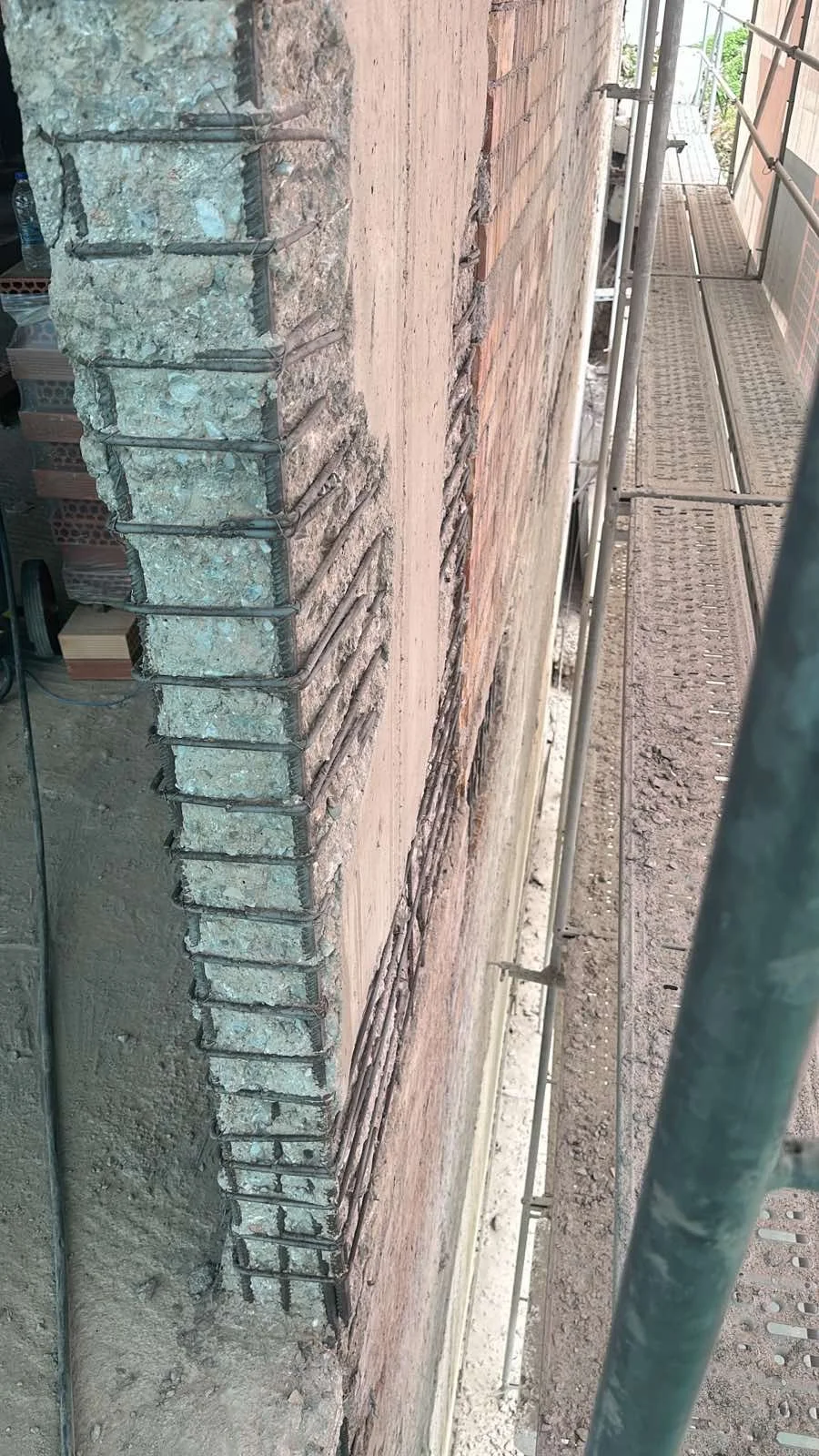 Construction site showing a brick wall with exposed rebar and scaffolding on the side.