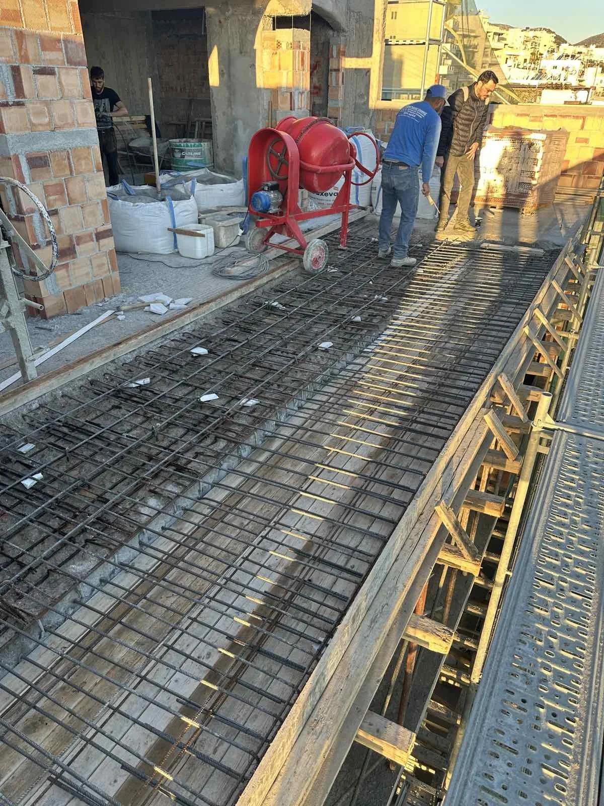 Three construction workers on a building site working on concrete reinforcement with steel rebar in preparation for pouring concrete. There are construction tools and materials around.