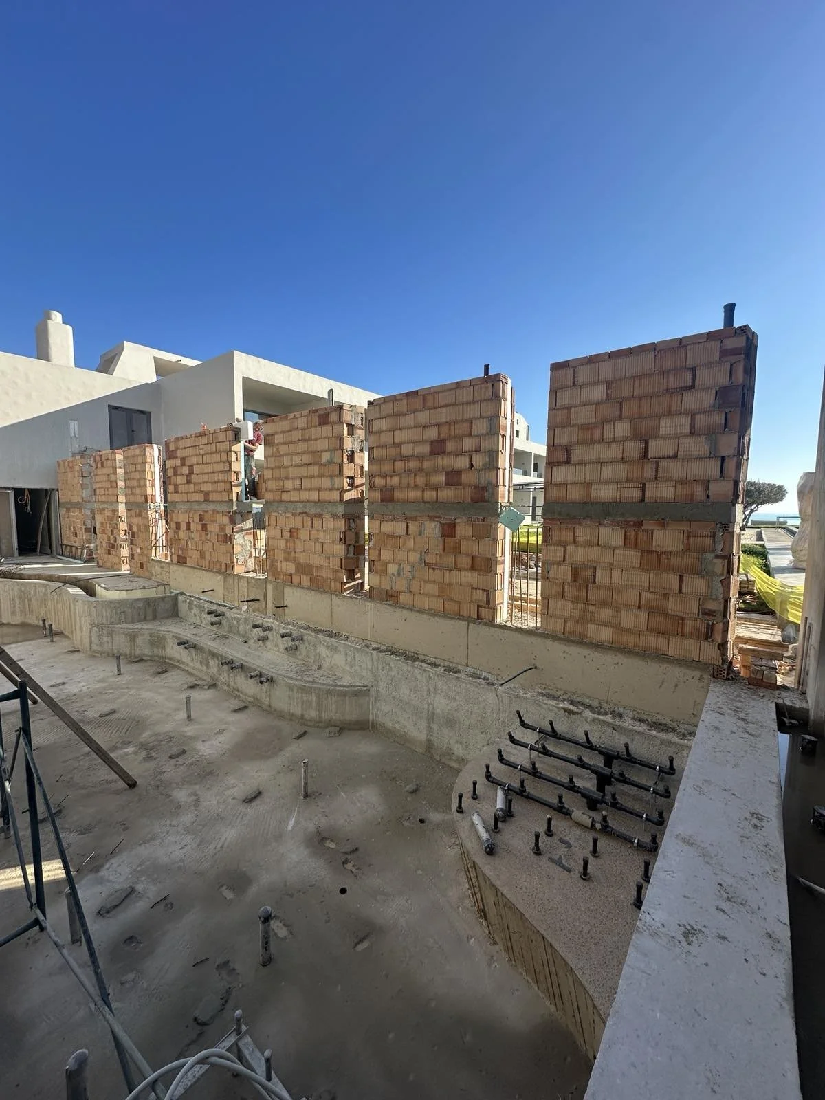 Construction site with brick walls, a clear blue sky, and residential buildings in the background.