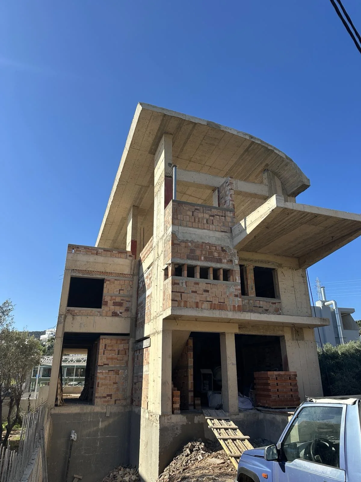 Under construction multi-story building with exposed brick and concrete, scaffolding, and a truck parked in front, against a clear blue sky.
