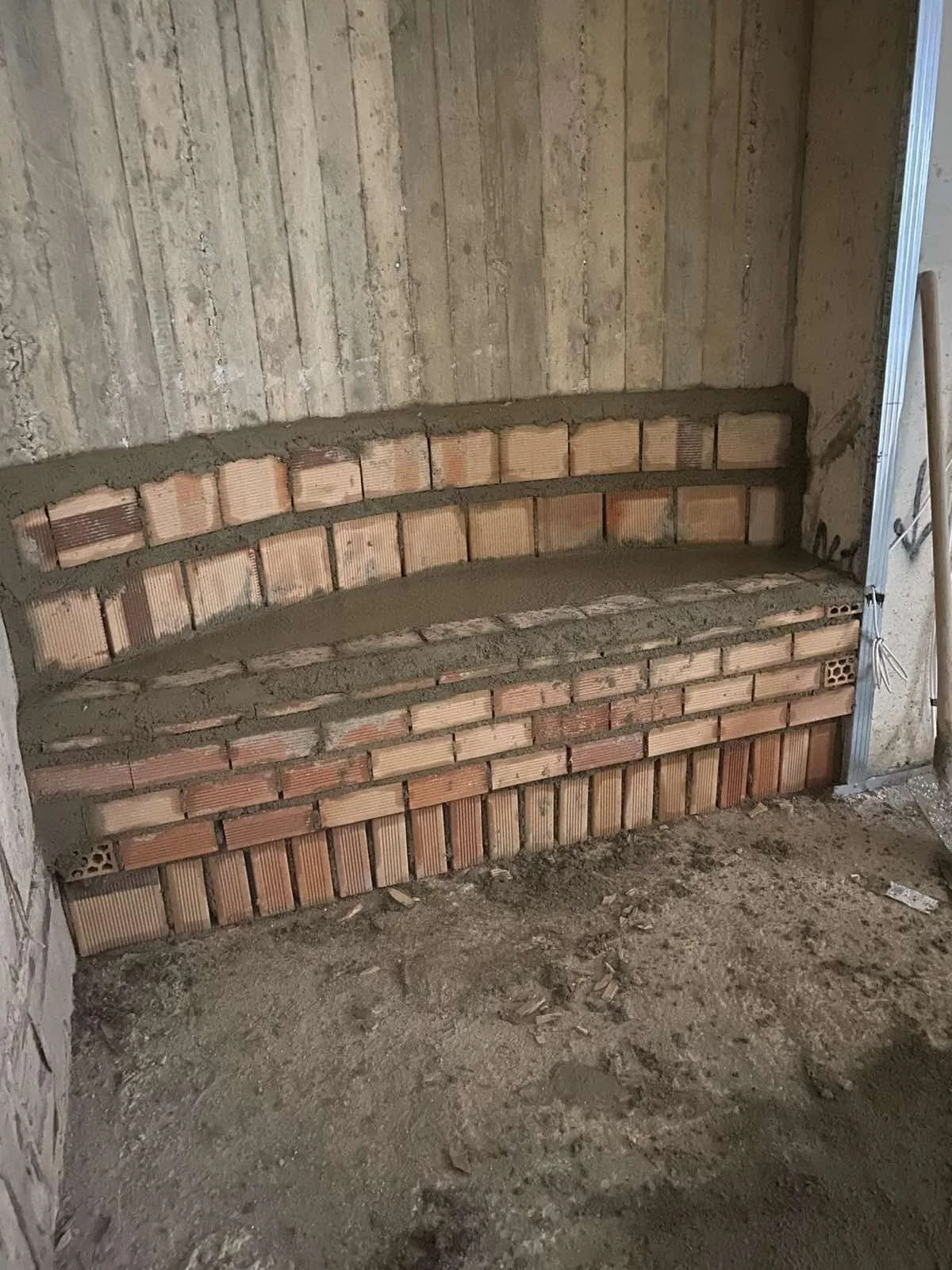 A brick fireplace under construction with multiple layers of bricks and mortar, with a rough unfinished floor and walls.
