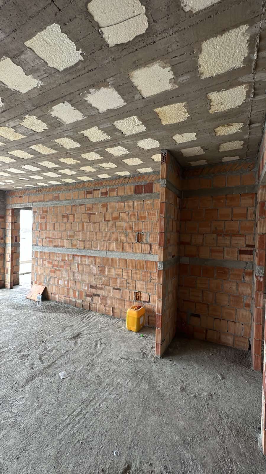 Interior of a building under construction with brick walls and a concrete ceiling with insulation patches.