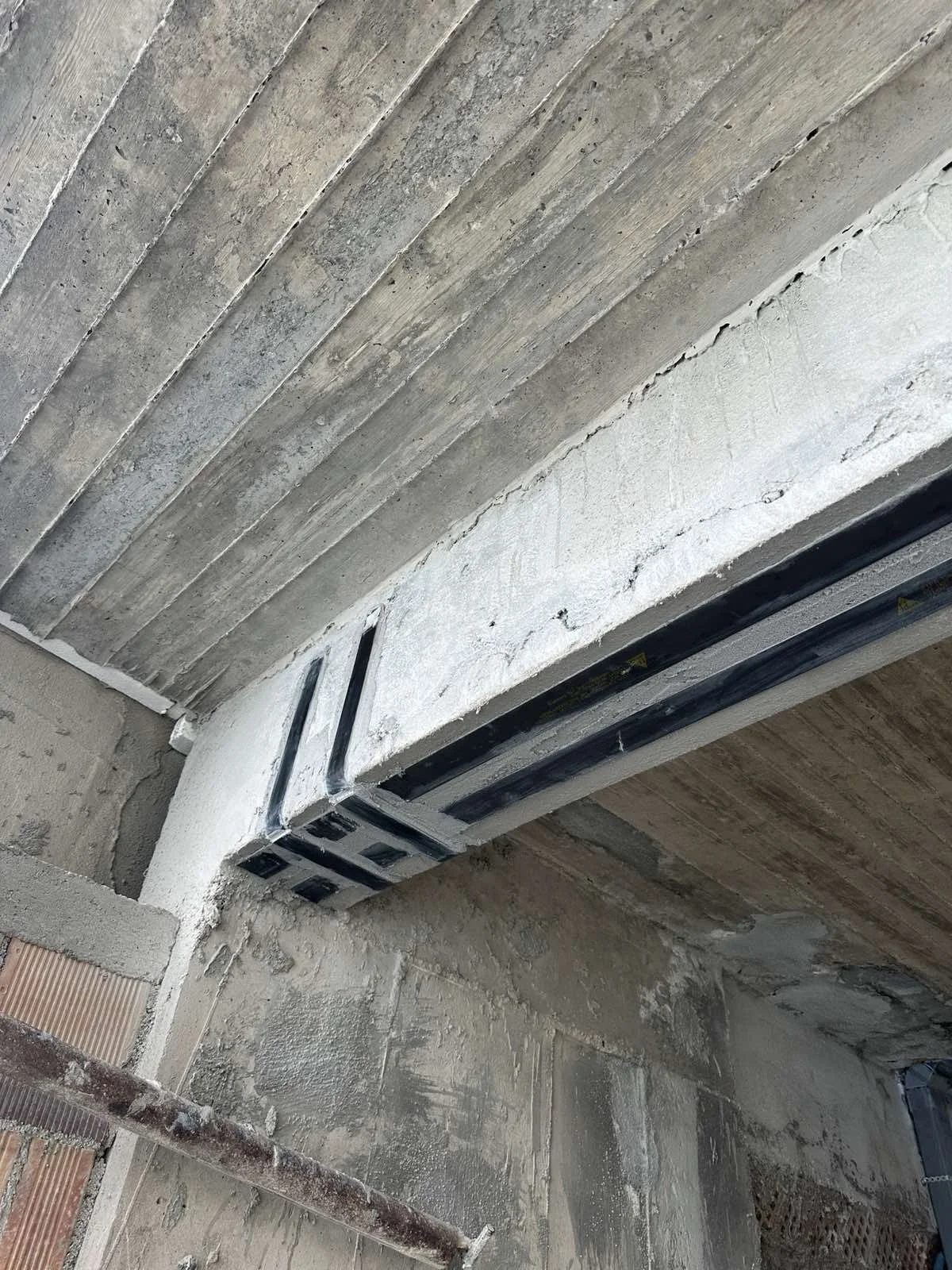 Construction site showing concrete ceiling with black cables or pipes installed in a wall opening.