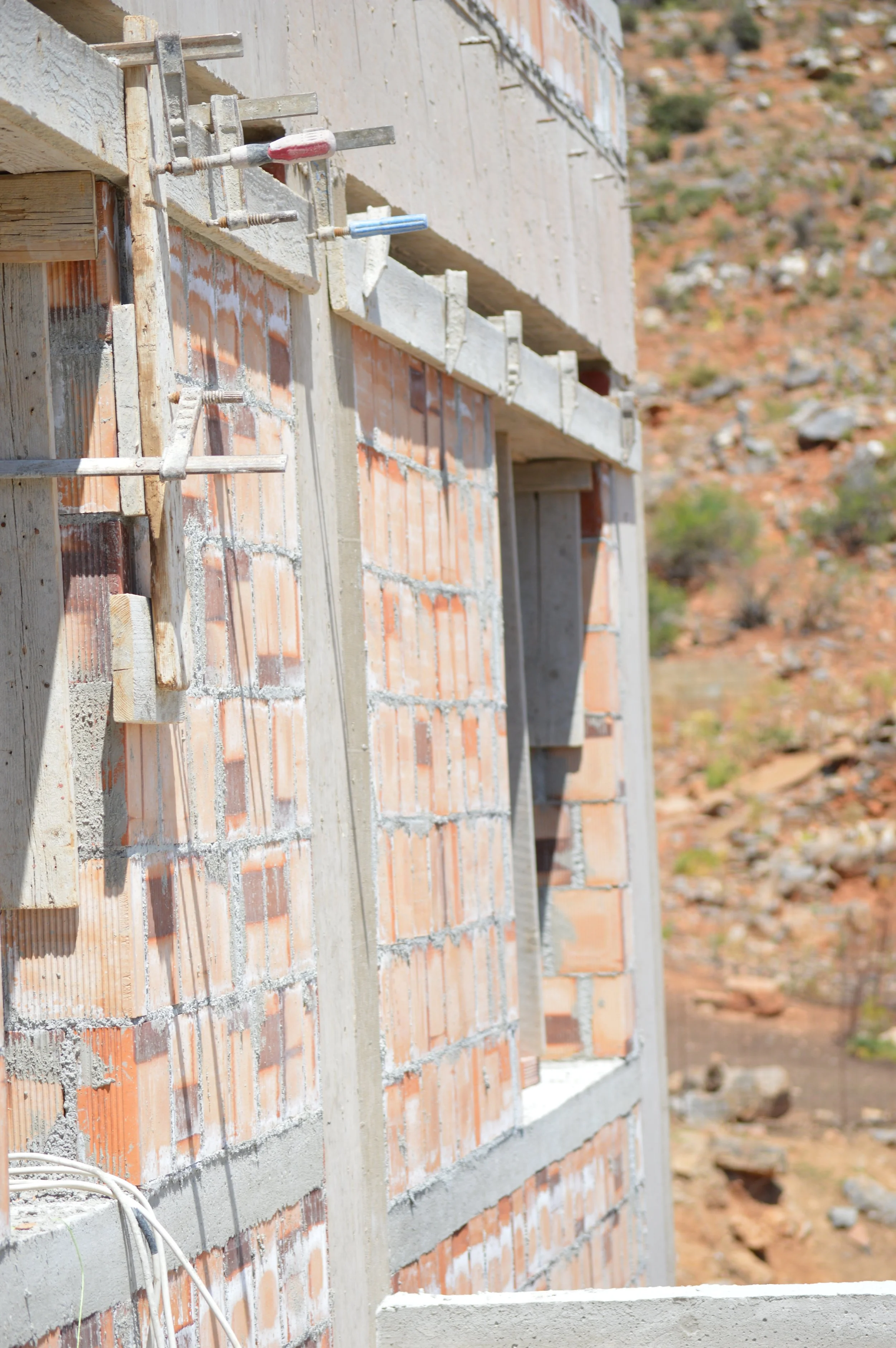 Exterior of a brick building under construction with metal scaffolding and wooden supports, on a construction site in a desert landscape.