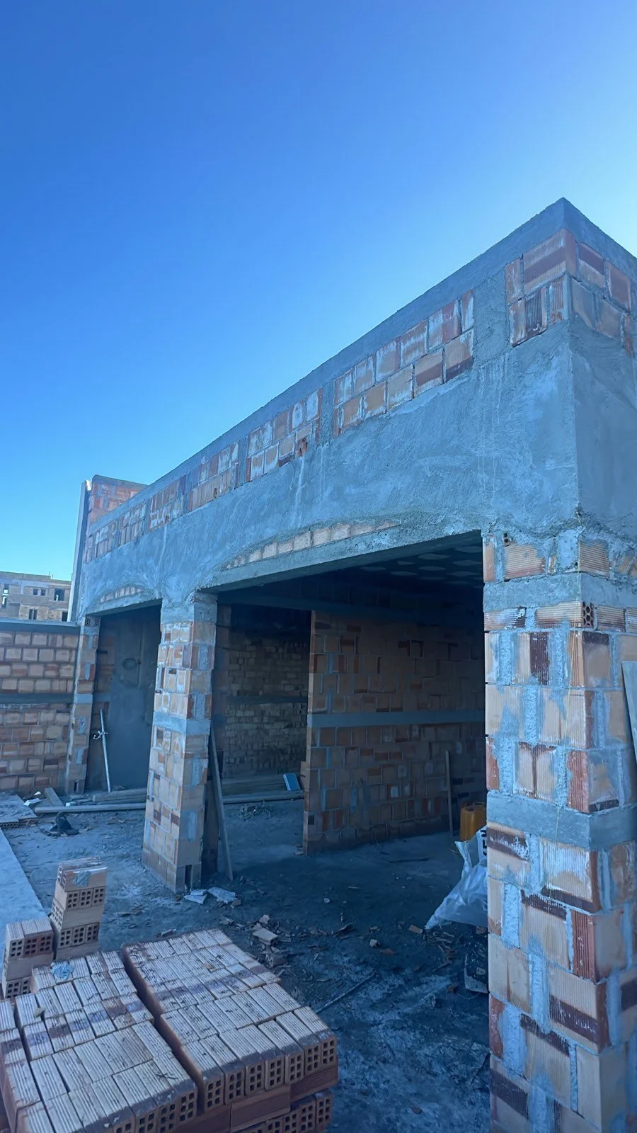 Under-construction brick building with an open garage, on a clear blue day.