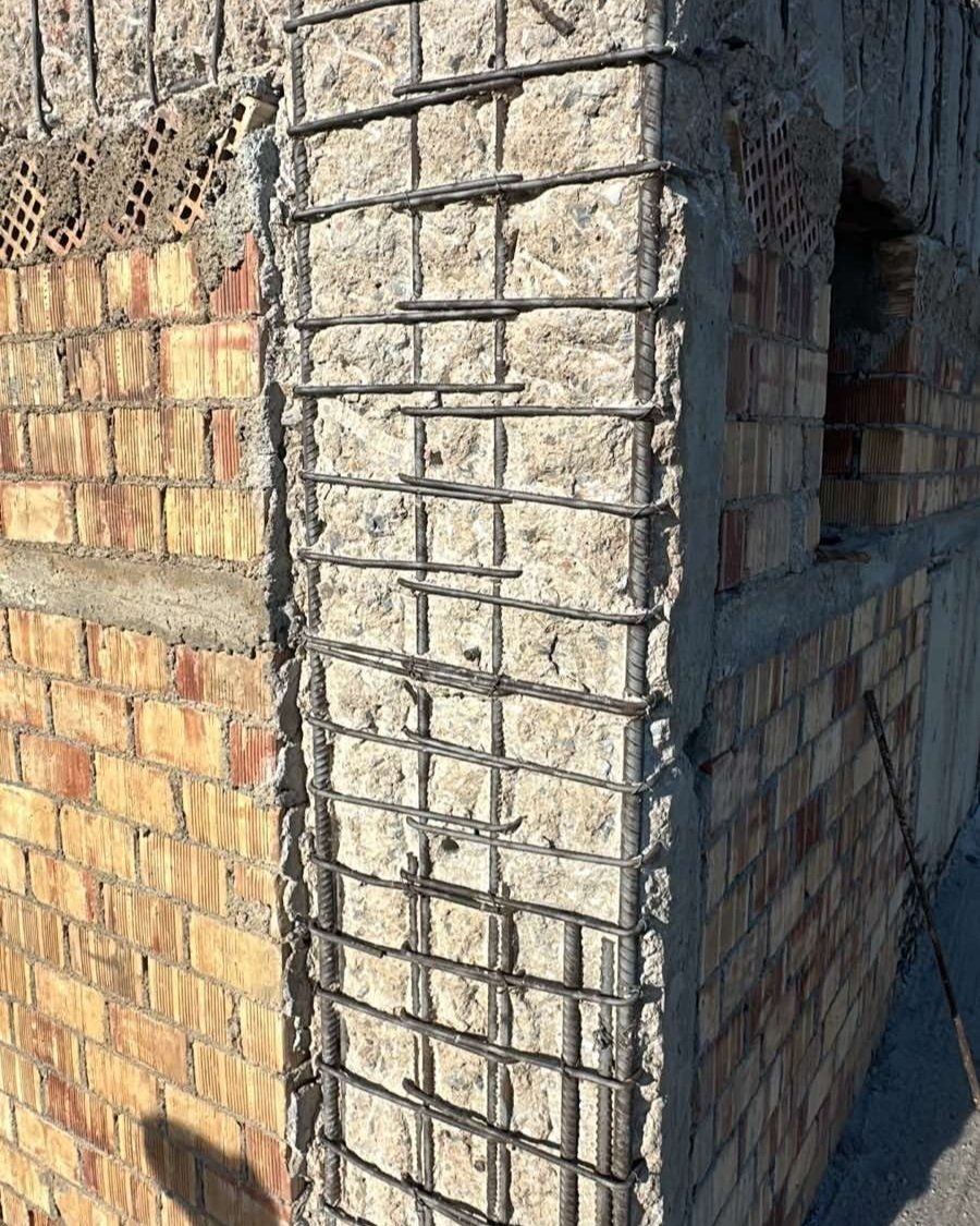 Close-up of a concrete wall with exposed rebar, adjacent to a brick wall under construction.