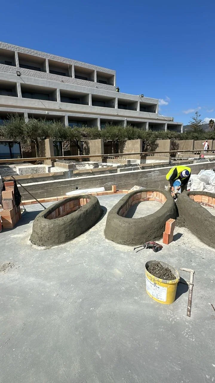 Construction site with a worker shaping concrete structures for landscaping in front of a modern building with multiple balconies.