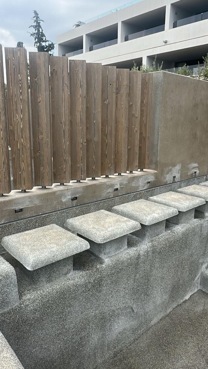 Concrete stairs with four stone treads, a wooden fence, and a modern white residential building in the background.