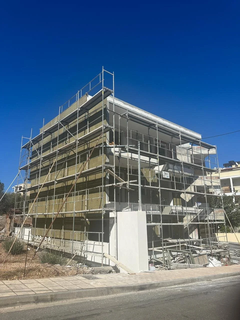 Construction site with a building surrounded by scaffolding during exterior renovation or construction, against a clear blue sky.