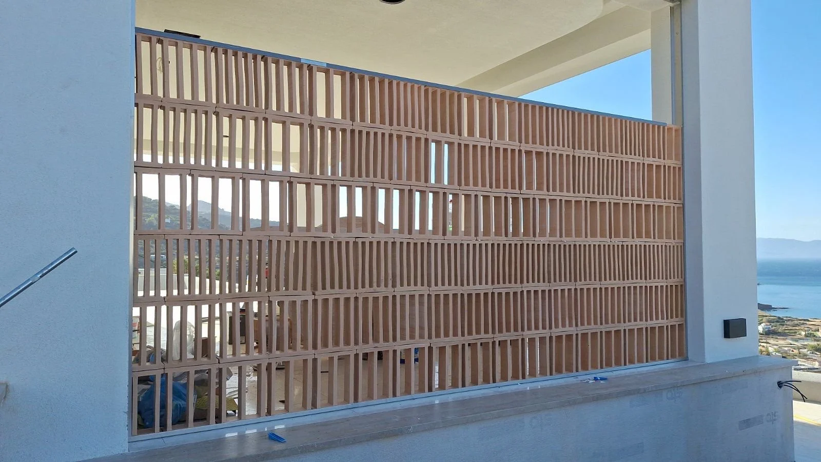 View of a wooden slat privacy wall on a balcony with the ocean and distant hills in the background.
