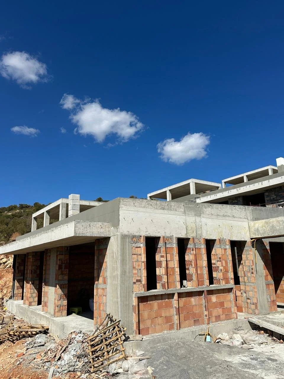 Construction site of a building with brick walls and concrete beams, under a blue sky with scattered clouds.