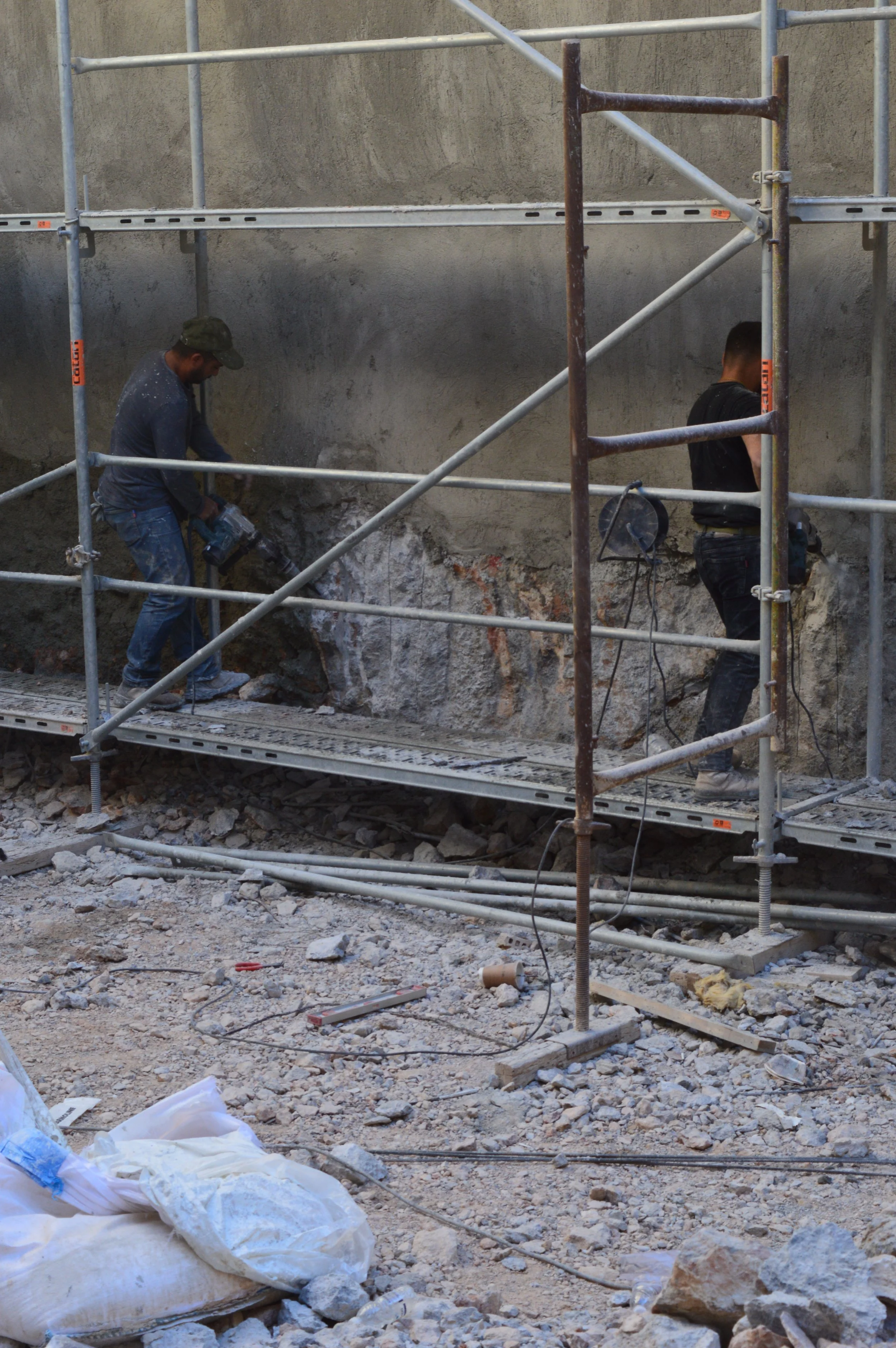 Two construction workers working on a building renovation, using tools on a partially exposed wall with scaffolding around them.