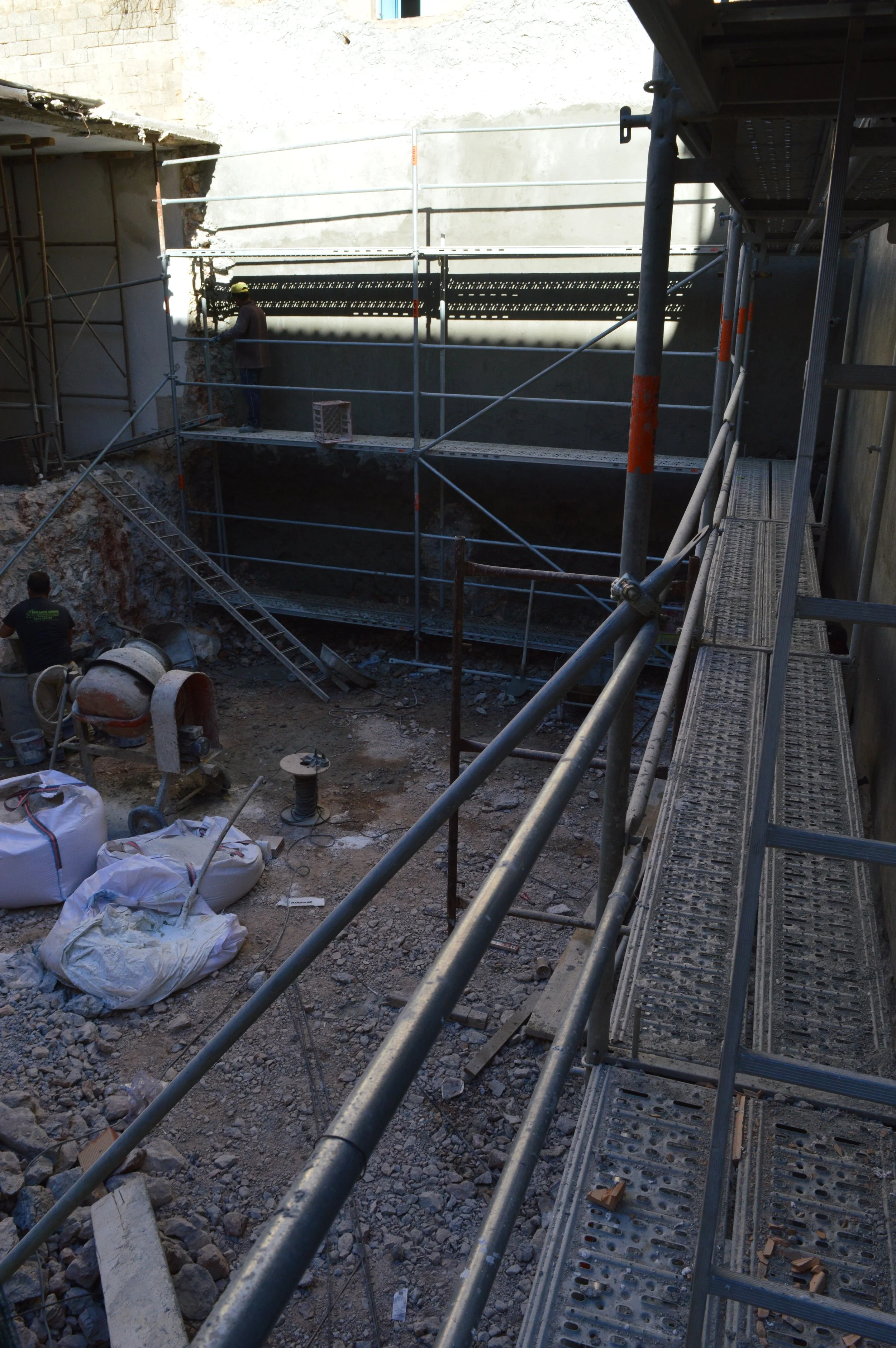 Construction site with scaffolding, workers, concrete mixer, and building materials.