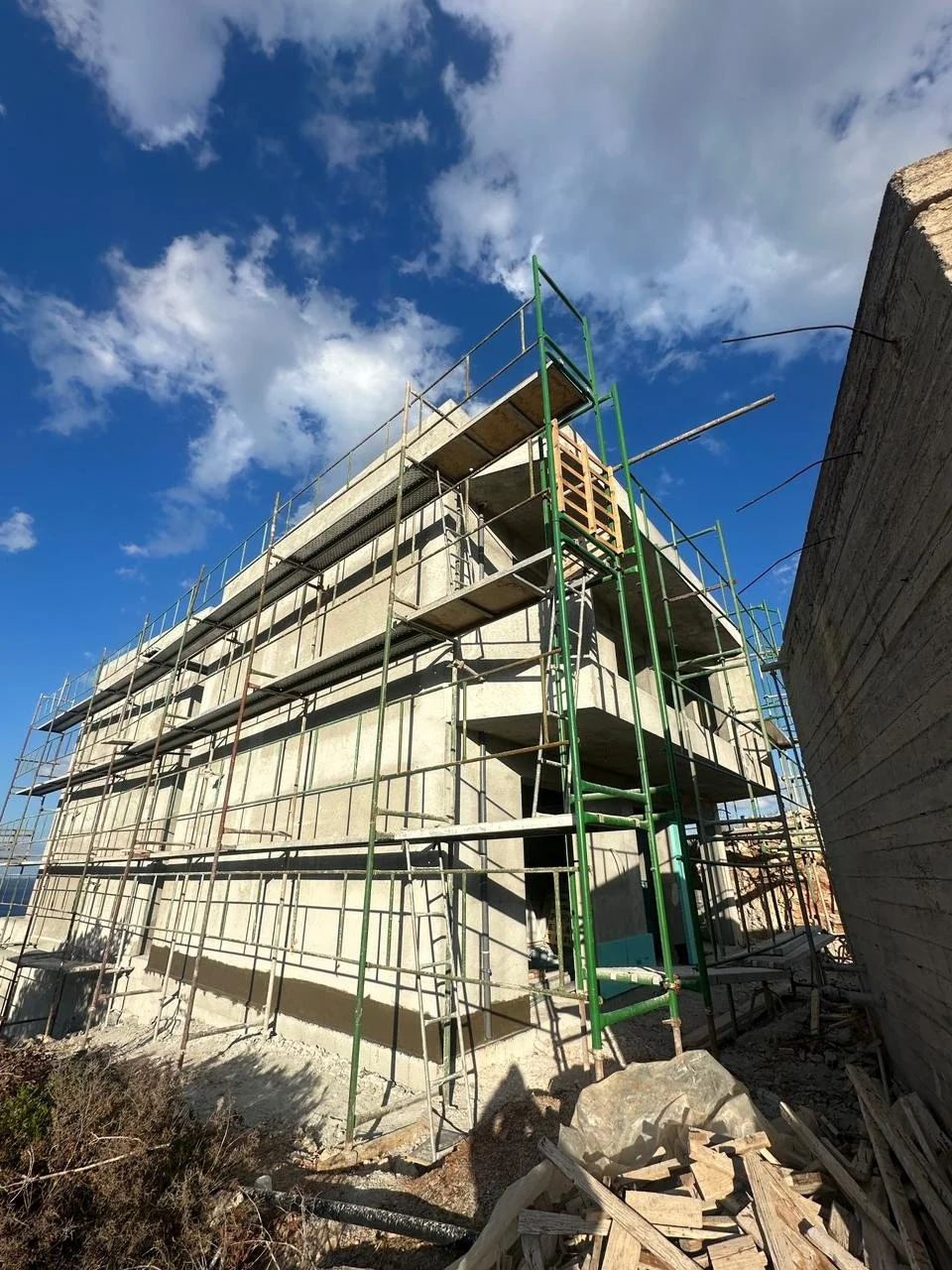 Construction site with scaffolding around a multi-story concrete building under blue sky with clouds.