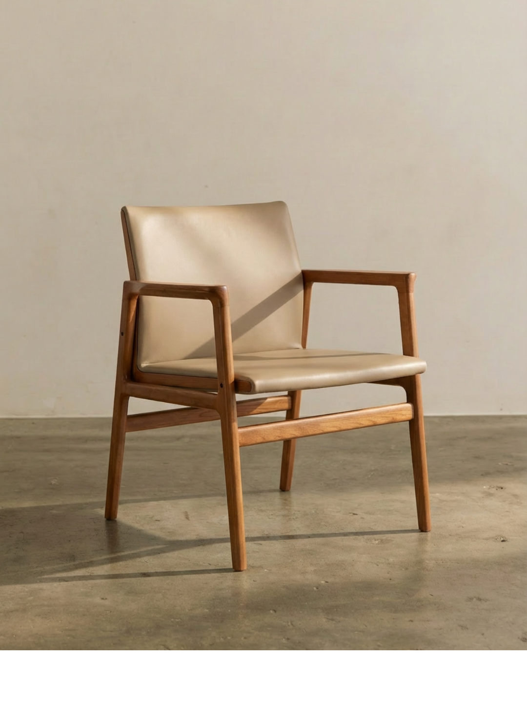 A modern armchair with wooden frame and beige cushioned seat and backrest, placed against a plain wall on a concrete floor.