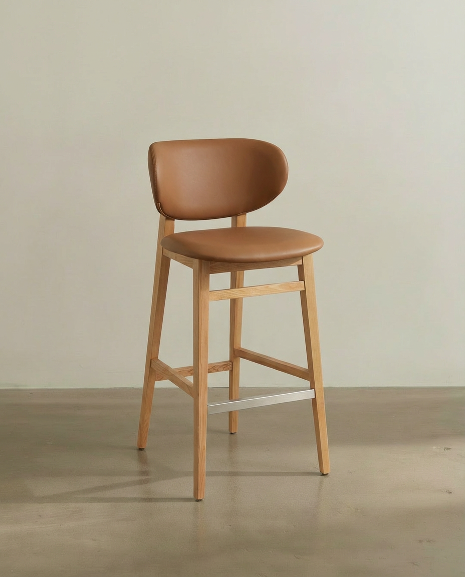 A modern bar stool with a light wood frame, brown leather seat and backrest, set against a plain light-colored wall and wooden floor.