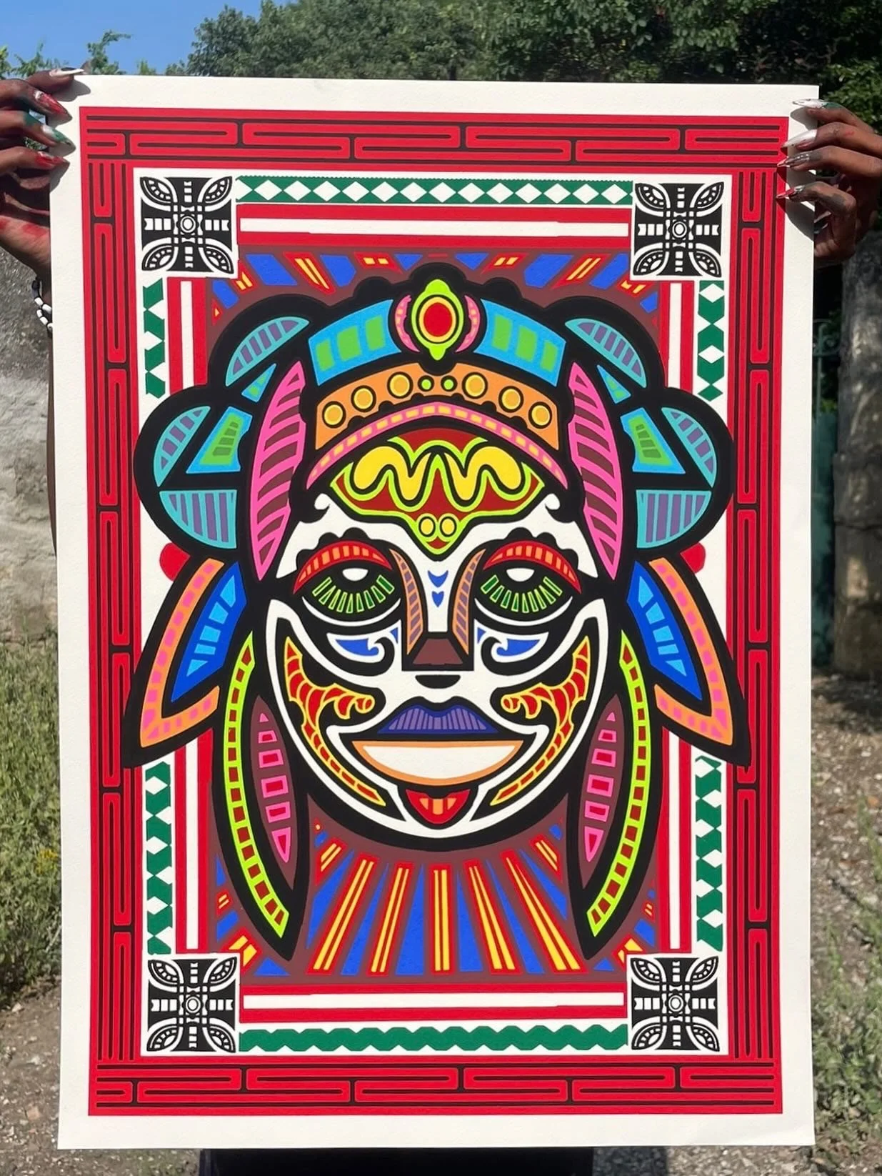 Une affiche colorée représentant une figure stylisée d'un masque traditionnel, avec des motifs géométriques et des couleurs vives telles que le rouge, le vert, le bleu, le jaune, le rose et le violet, encadrée par une bordure rouge avec des motifs en noir et blanc.