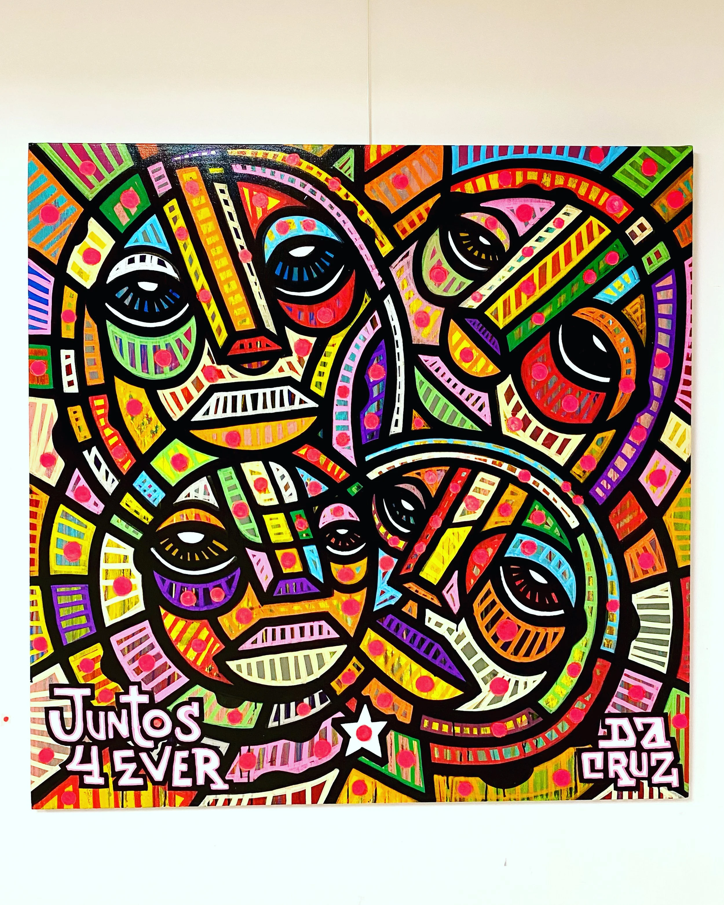 Une peinture colorée représentant plusieurs visages stylisés avec des traits noirs, des couleurs vives et des motifs géométriques.