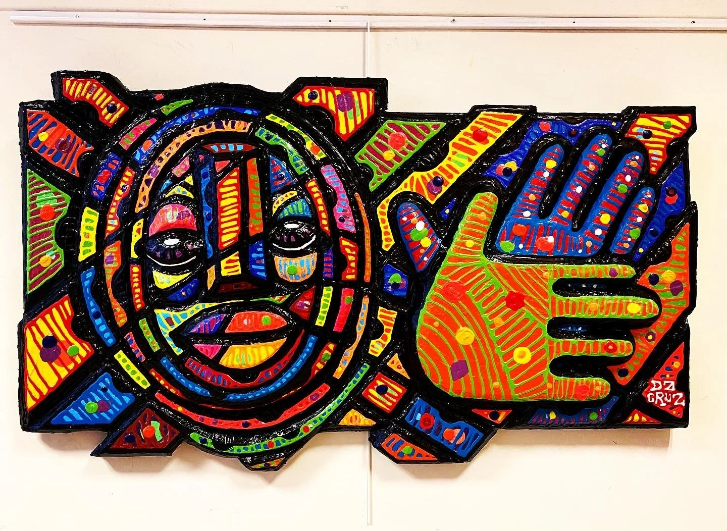 Une œuvre d'art murale colorée représentant un visage stylisé avec un œil, un nez et une bouche. À droite, une main stylisée avec doigts expressifs, le tout entouré de motifs géométriques et de couleurs vives.