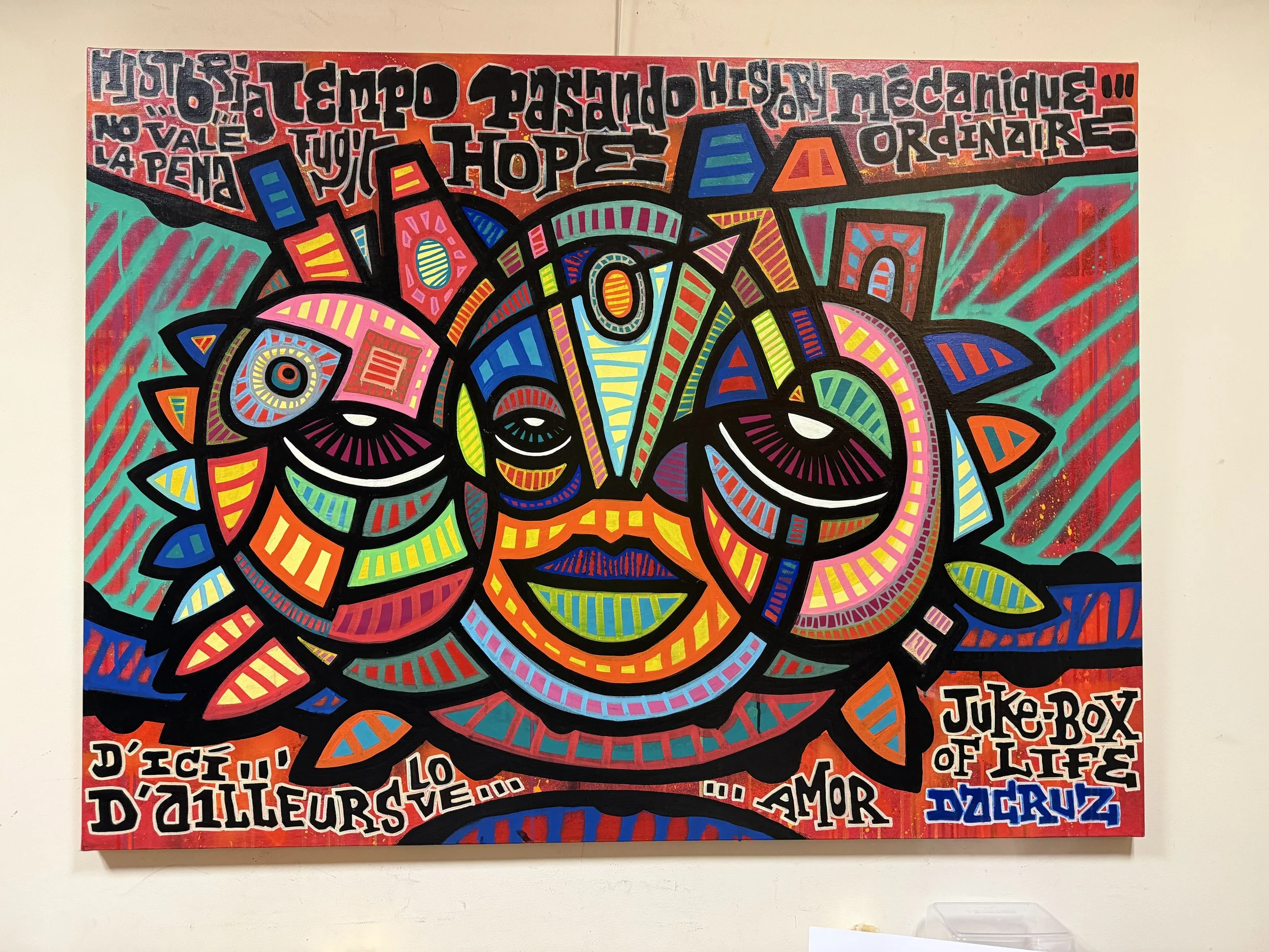 Une œuvre d'art colorée représentant un visage stylisé avec des formes géométriques, des yeux grands et une bouche souriante, entouré de textes en français et en anglais.